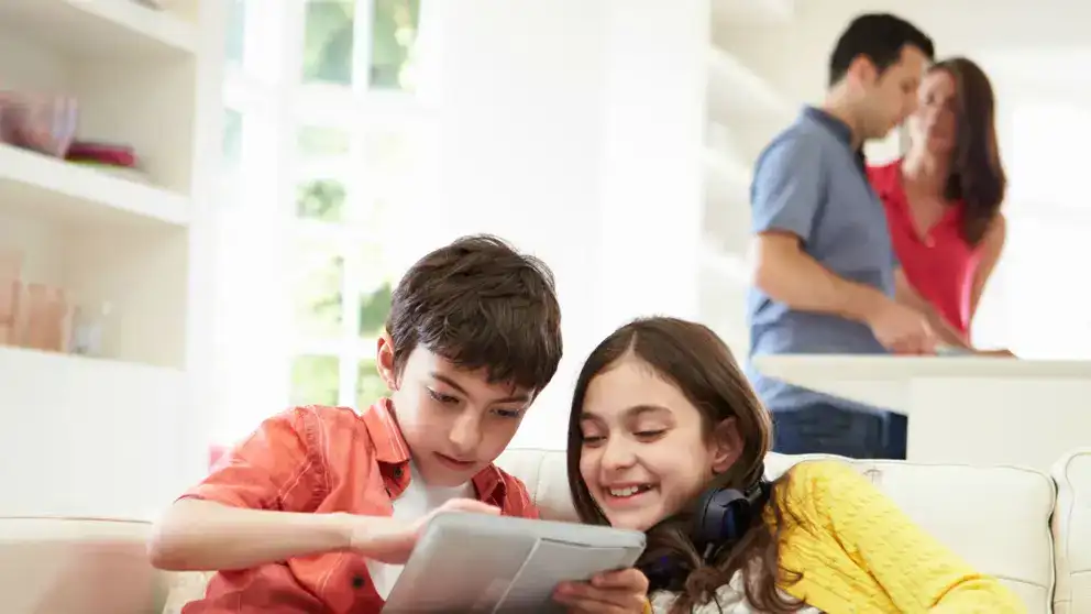 Frère et soeur jouant sur tablette tandis que les parents préparent le diner