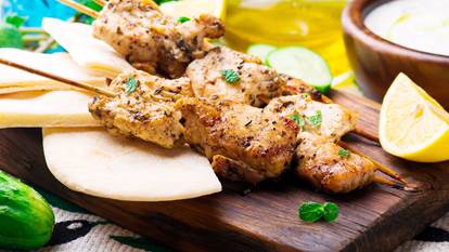 Chicken souvlaki on a cutting board with lemon and dip