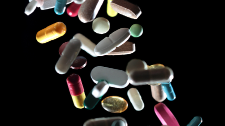 Pilules de toutes couleurs, formes et tailles tombant devant un fond noir