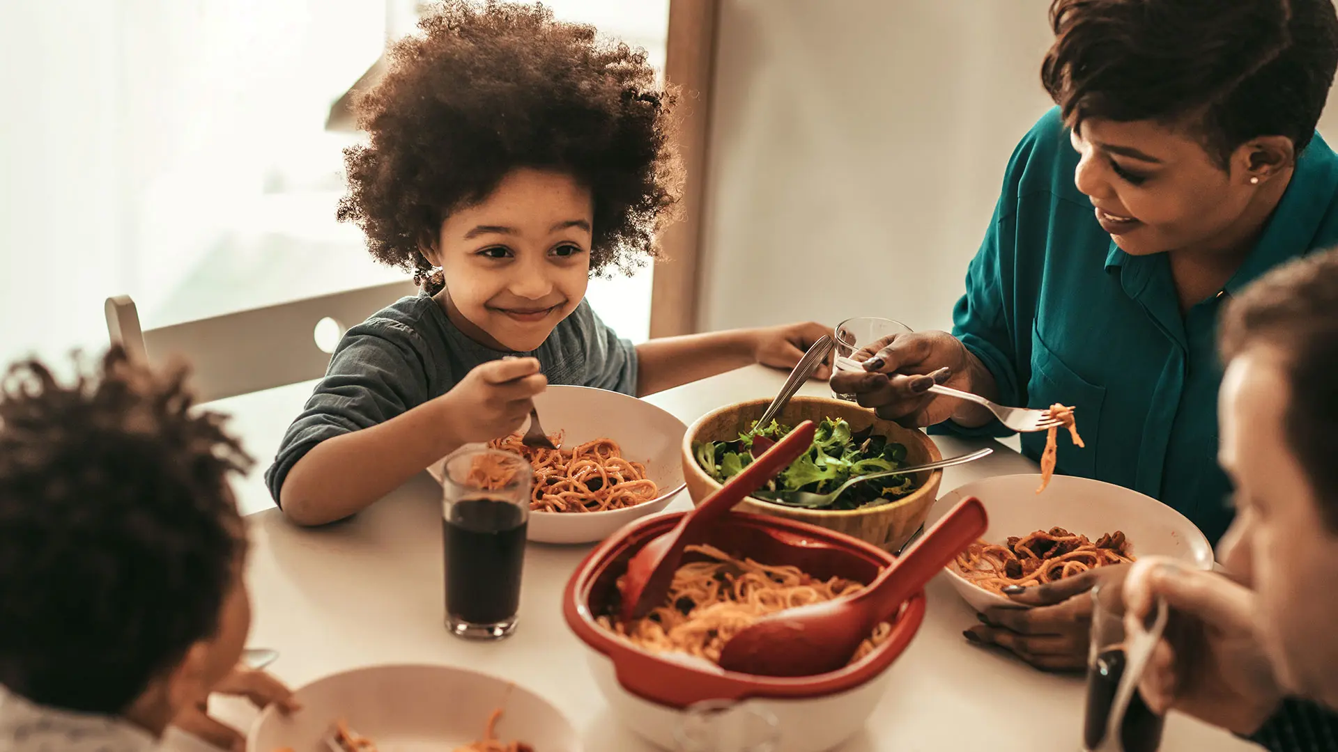 Enfant souriant à leur famille autour de la table du dîner, manger des spaghettis