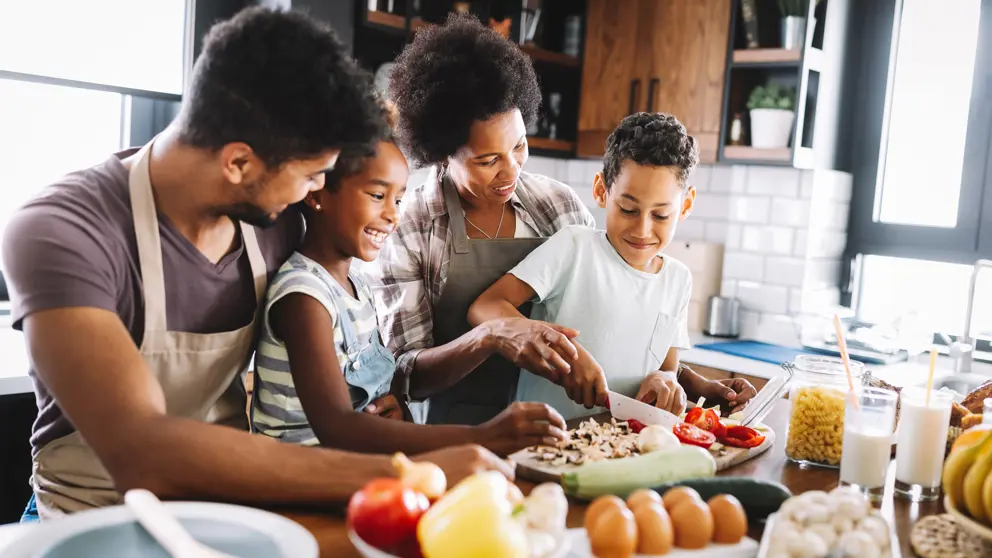 Deux adultes et deux enfants préparent un plat ensemble dans une cuisine.