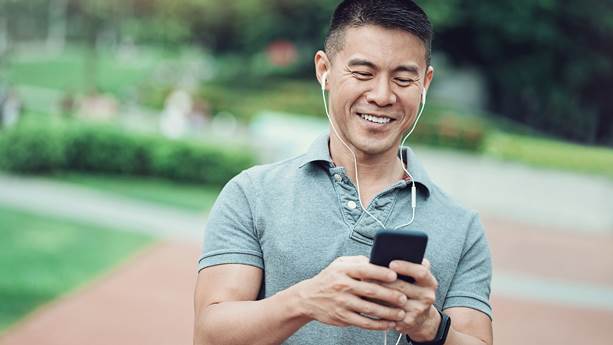Dans un parc, un homme souriant manipule son téléphone cellulaire.