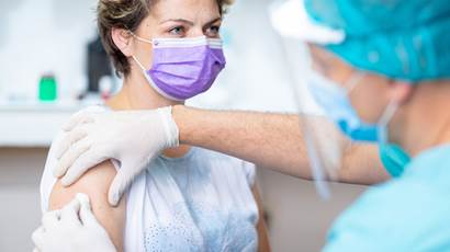 Une patiente porte un masque protecteur en attendant la vaccination avec un médecin en gants chirurgicaux désinfectant son bras.