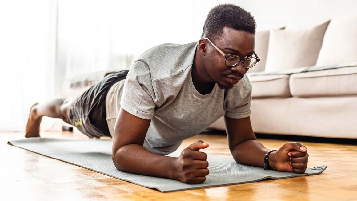 Un homme faisant l’exercice de la planche sur un tapis à la maison.