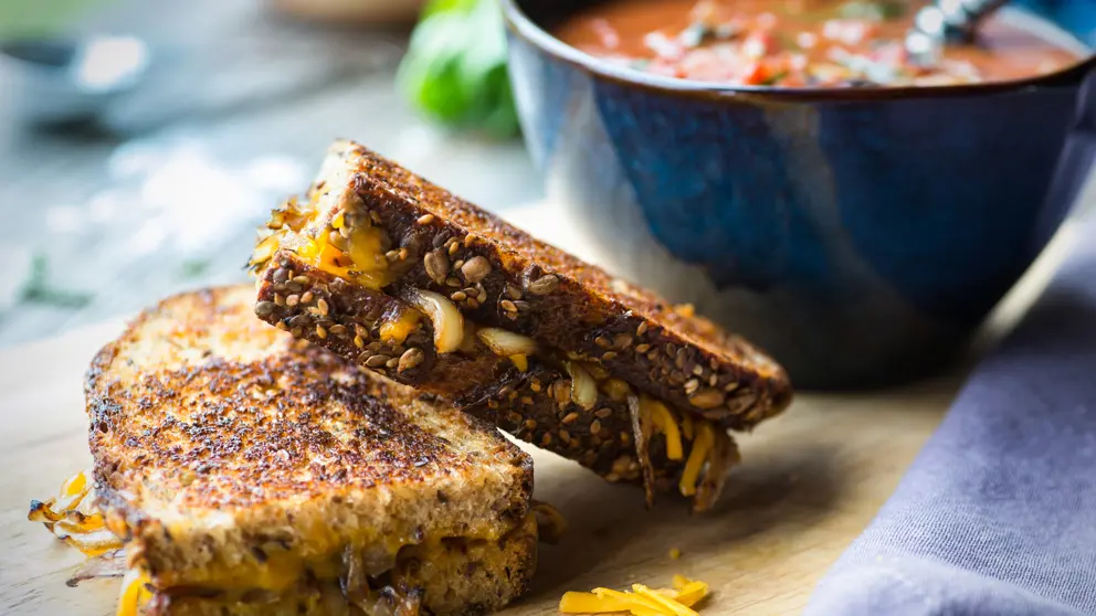 Soupe à la tomate fraîche avec un sandwich au fromage et à l’oignon grillé sur une planche à découper en bois