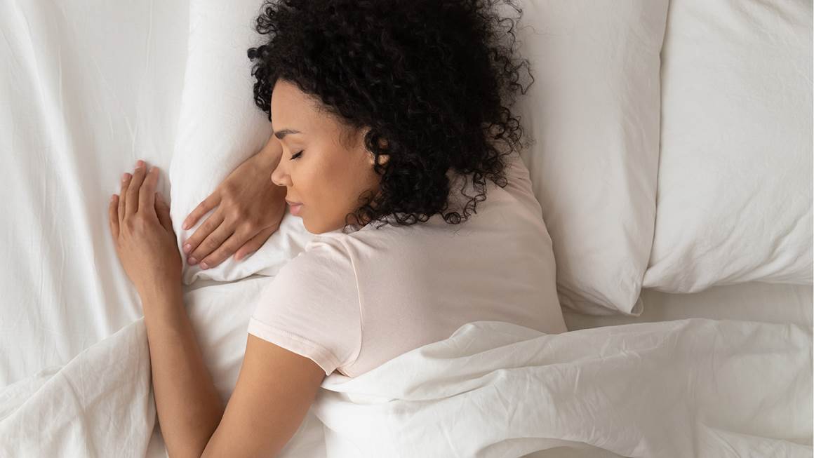 Une jeune Afro-Américaine sereine, confortablement endormie dans un lit aux oreillers et des draps blancs, vue de haut.