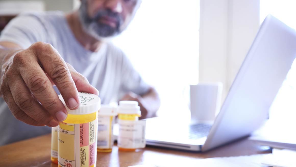 A man reaches for his prescriptions on a table.