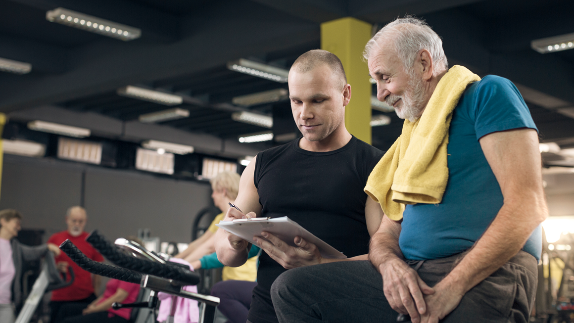 Older man reviewing his progress with trainer on a cycling bike