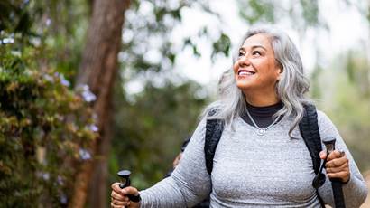 Smiling woman walking out doors holding hiking poles