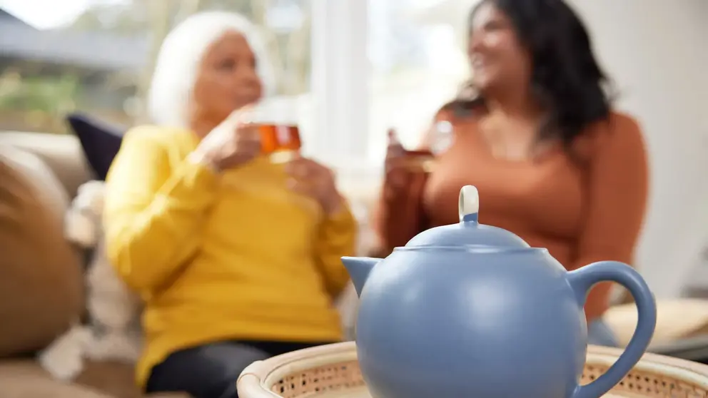 Une théière bleue avec deux femmes buvant du thé en arrière-plan.