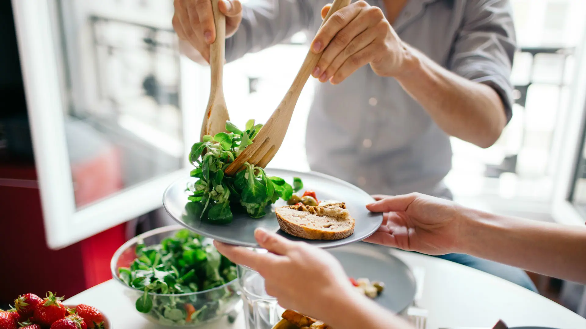 Un homme sert de la salade sur une assiette blanche avec du pain.