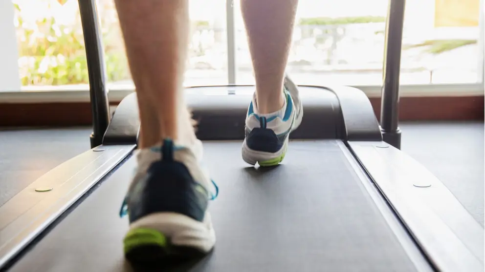 Gros plan des pieds d’un homme qui court sur un tapis roulant.
