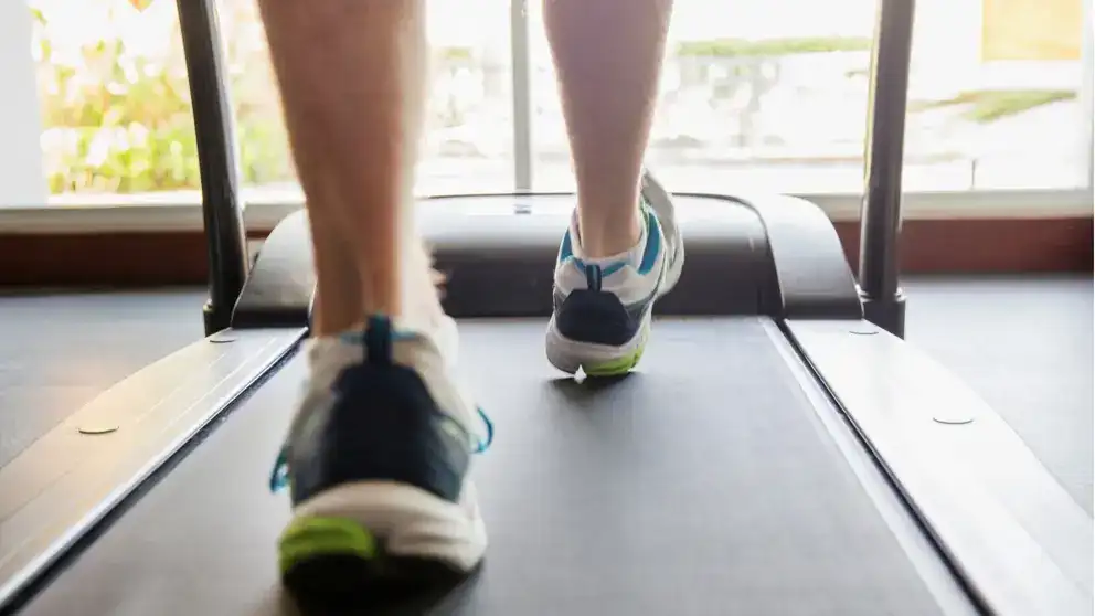 Gros plan des pieds d’un homme qui court sur un tapis roulant.