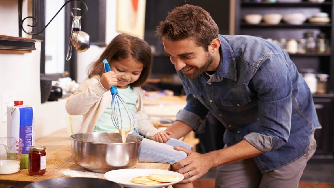 Un père et une fille sourient en cuisinant ensemble sur le comptoir de la cuisine.