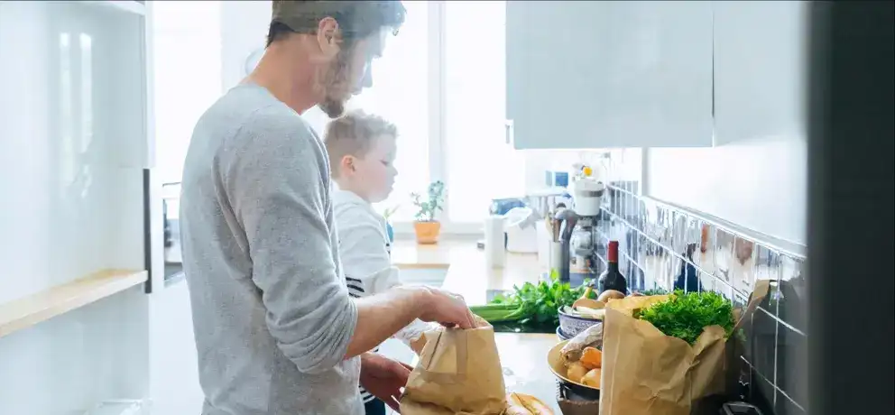 Dans une cuisine, un père et son fils rangent des articles d’épicerie.