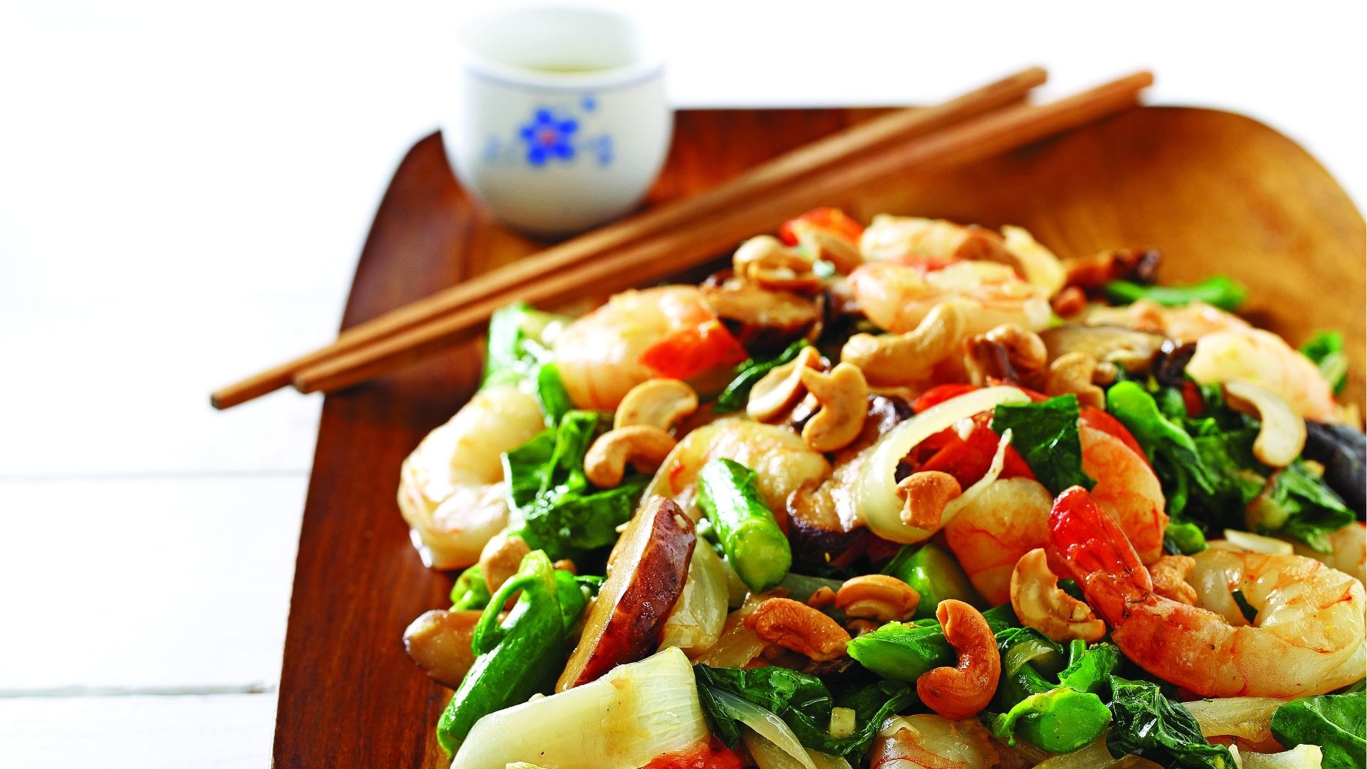 Crevettes, bok choy, poivrons rouges, noix de cajou sur planche de bois avec des baguettes