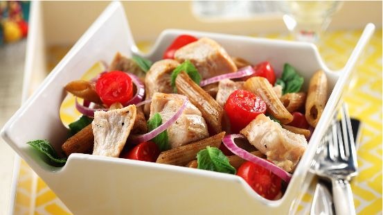 Salade de pâtes au poulet bistro dans un bol carré blanc avec une fourchette sur une nappe jaune