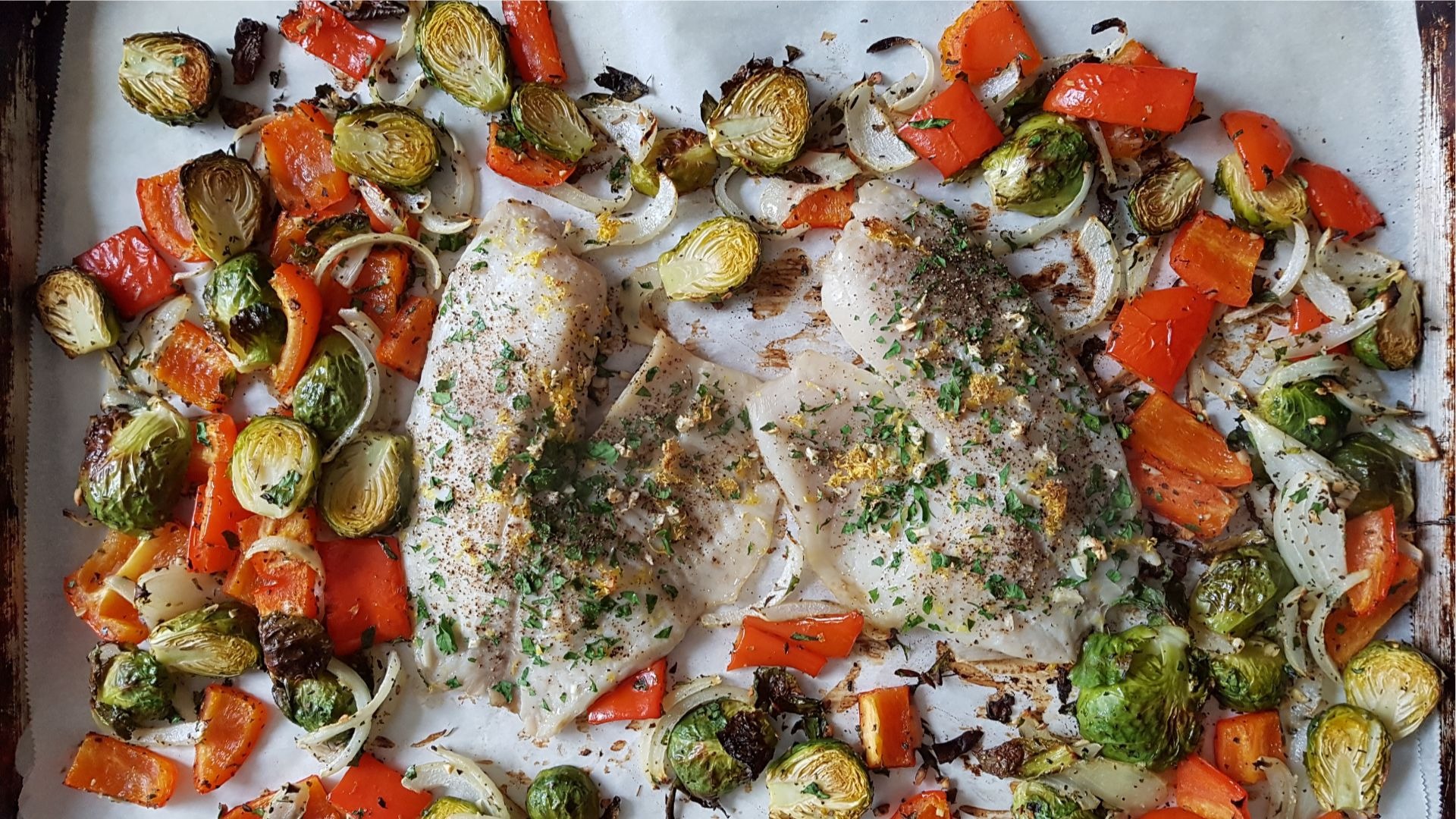 Filets de tilapia, choux de Bruxelles, poivrons rouges sur papier parchemin