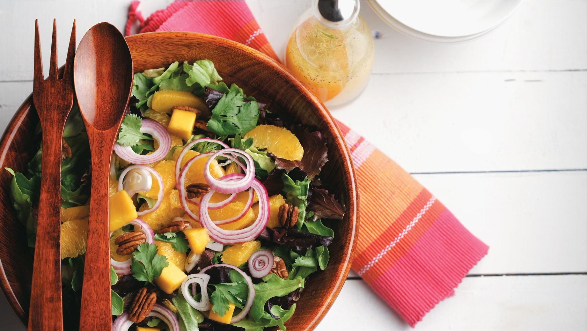 Salade de mesclun, mangue et noix de pacane dans un bol de bois avec utensiles de bois.