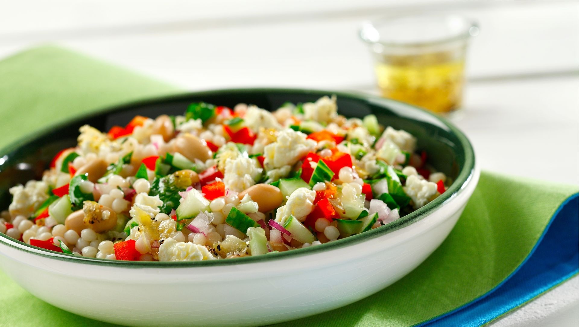 Salade de couscous perlé avec feta et romarin dans un bol blanc sur un set de table vert.