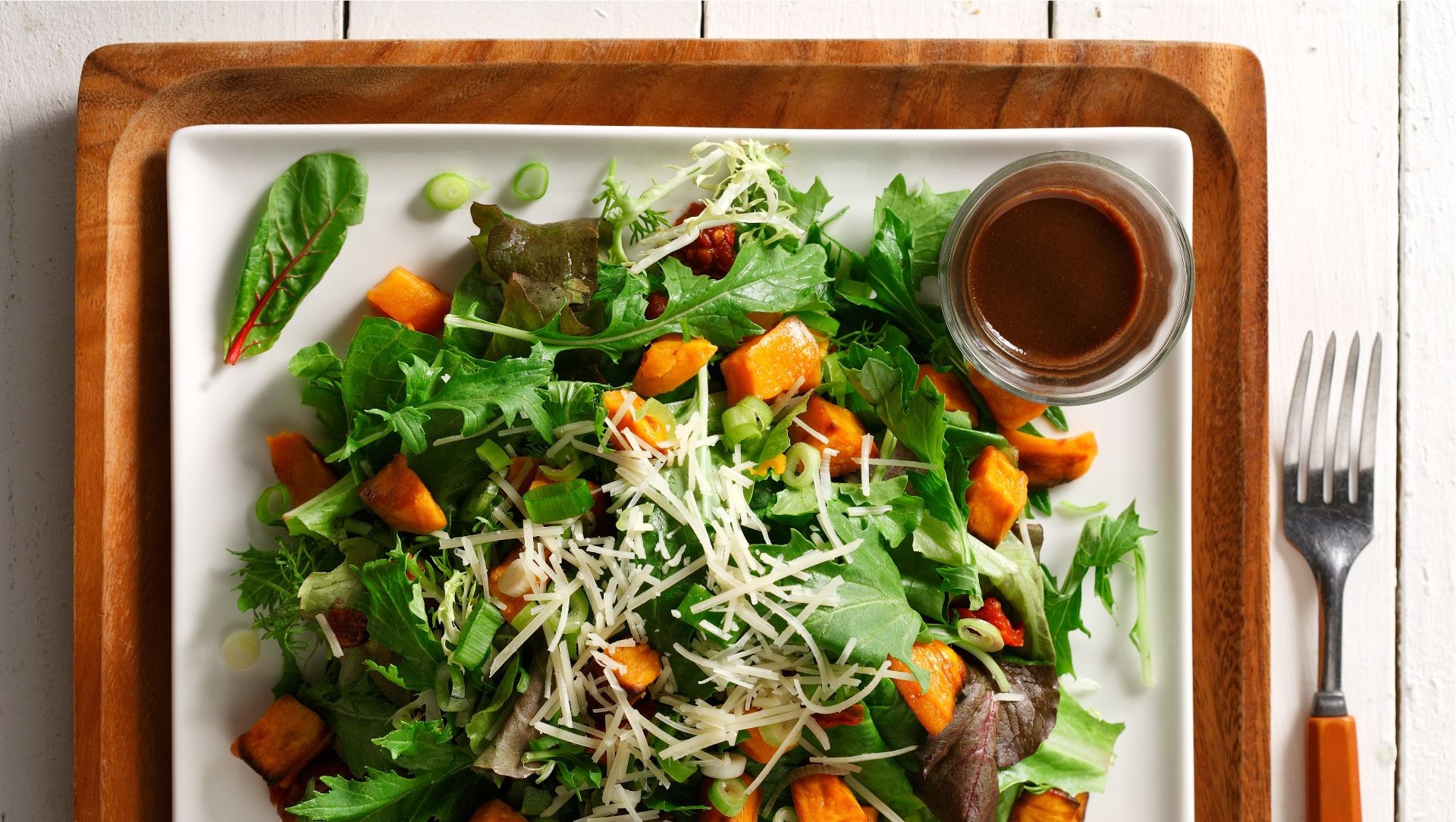 Salade tiède de patates douces, tomates séchées et roquette sur un plat blanc carré.