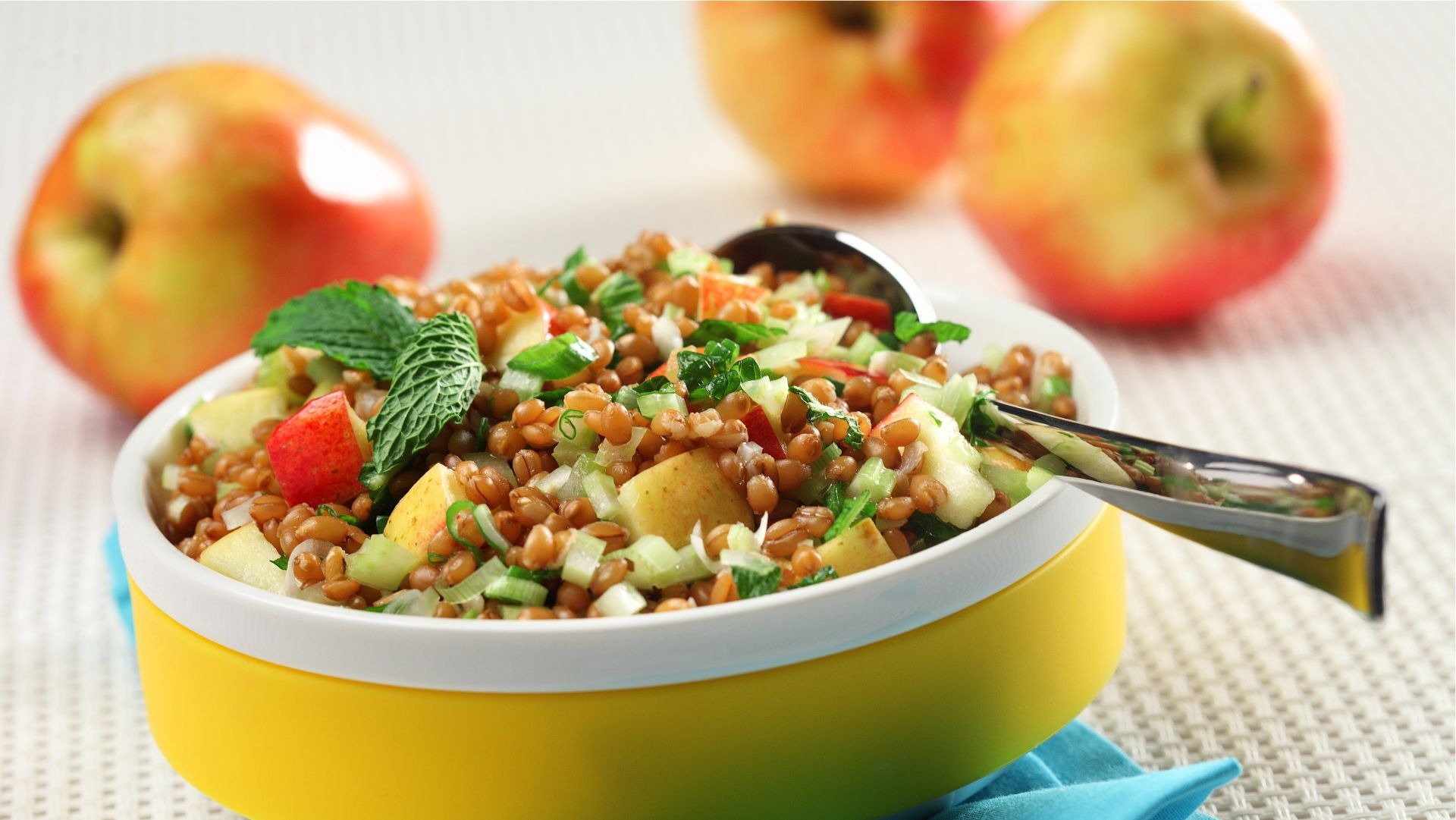 Salade aux grains de blé et pommes dans un bol jaune sur une serviette bleue