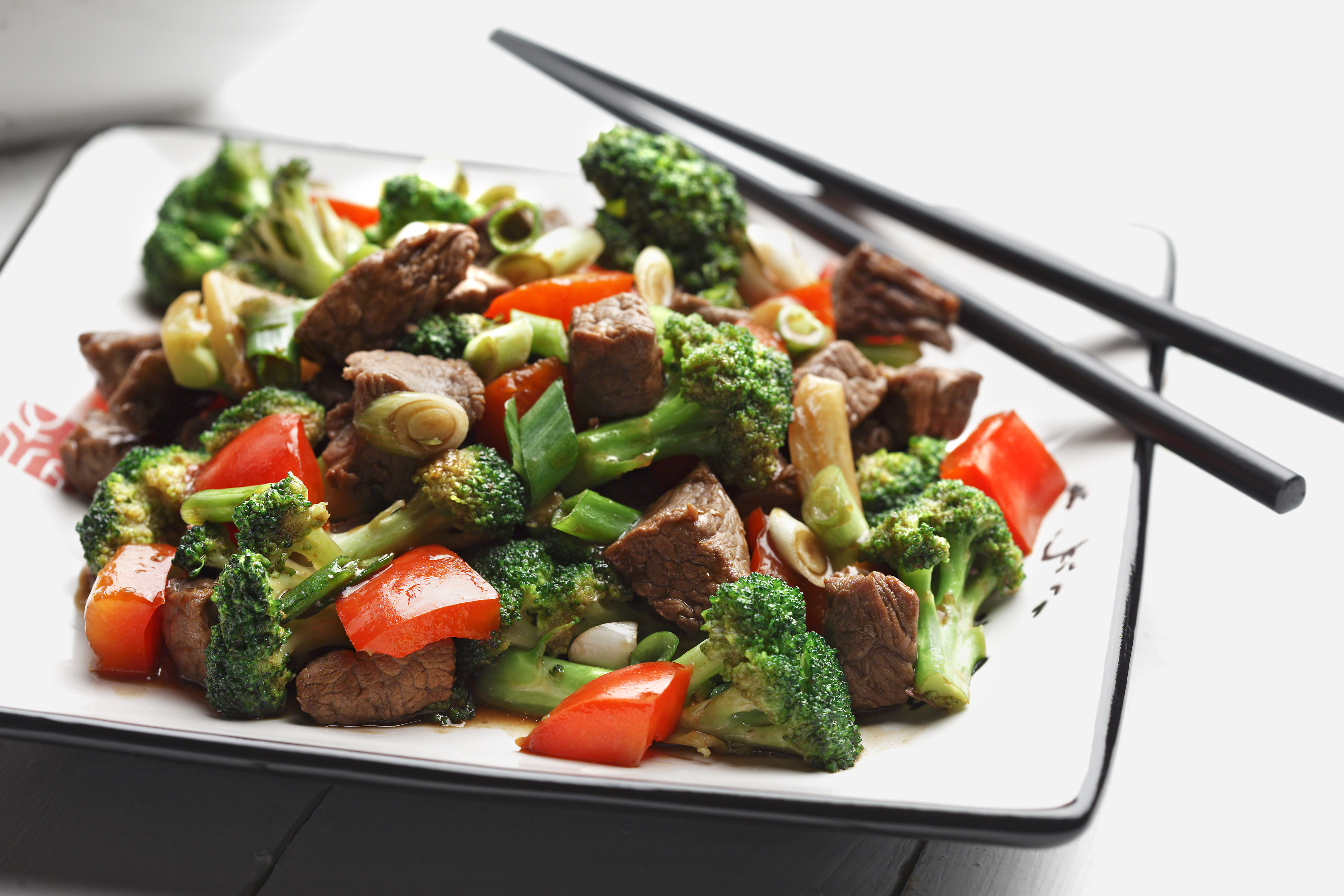 Sauté de brocoli, poivrons rouges et bœuf dans une assiette blanche avec des baguettes.
