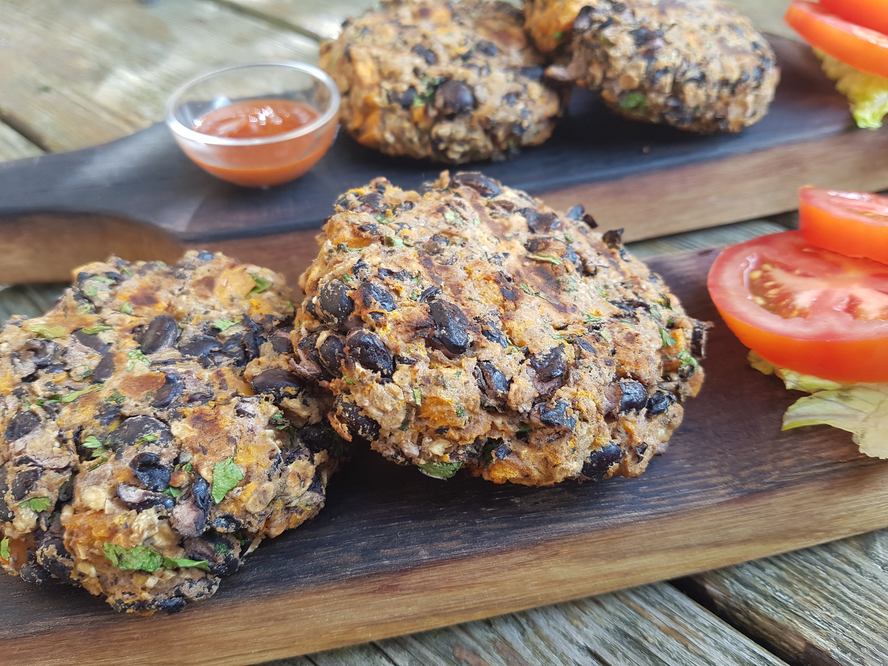 Galettes de hamburger de patates douces et de haricots noirs sur une planche avec des tomates