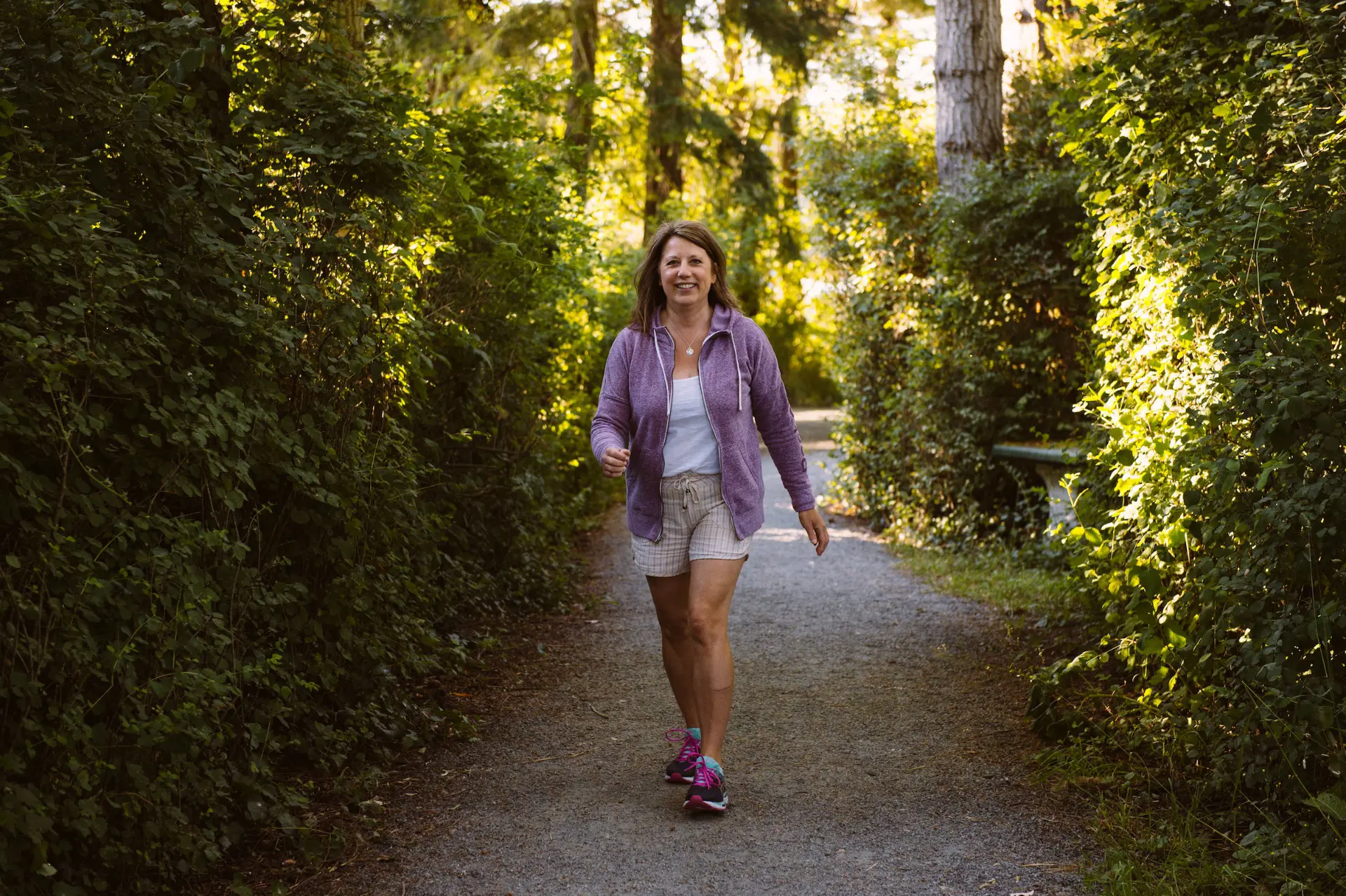 Tracy Bawtinheimer marche en forêt vêtue d’une veste mauve et de pantalons courts.