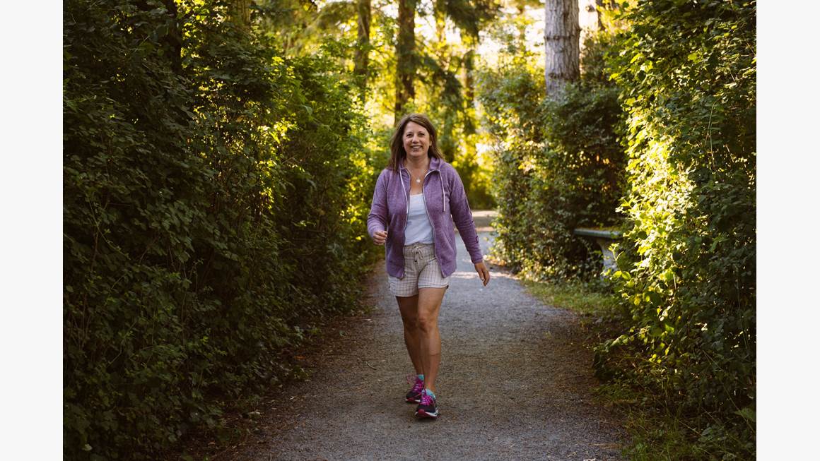 Tracy Bawtinheimer marche en forêt vêtue d’une veste mauve et de pantalons courts.