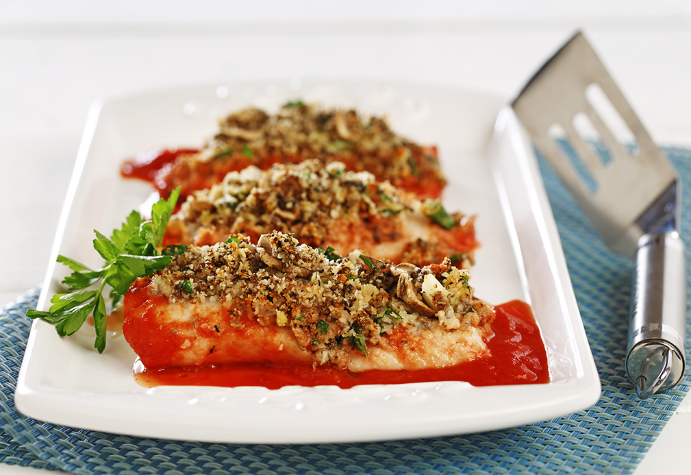 Poisson cuit surmonté d'herbes sur assiette blanche avec sauce rouge