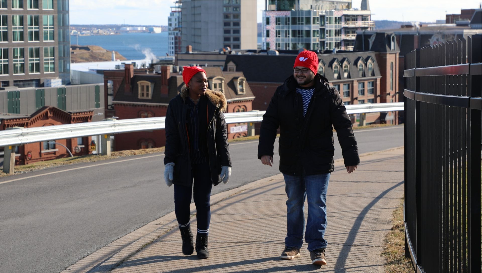 Deux bénévoles portant une tuque rouge marchent sur une rue principale.