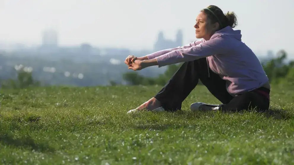 Jeune femme assise sur l'herbe dans les vêtements de sport paysage en arrière-plan