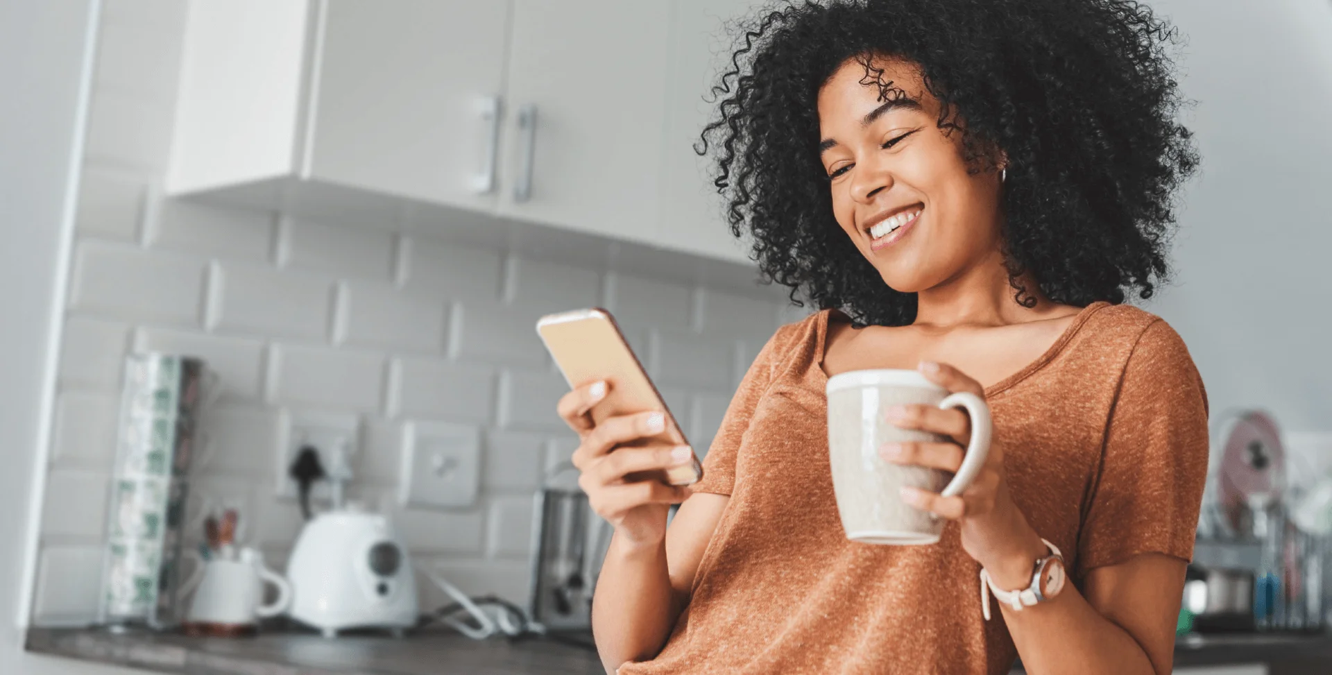 Une femme souriante tient une tasse de café et lit son téléphone