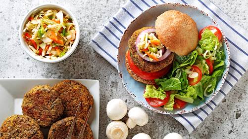 Burgers de courge aux champignons sur une assiette avec un petit pain, salade, tomates et champignons entiers sur le côté.