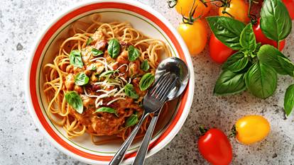 Rôti sauce tomate Linguini dans un bol avec l'argenterie et les tomates entières et des coupures de basilic sur le côté.
