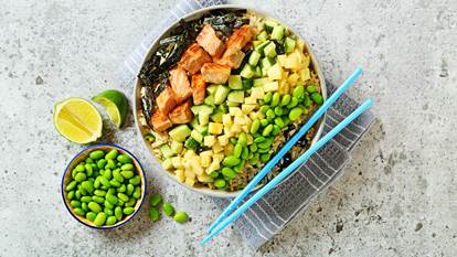 Salade style saumon poke dans un bol avec des baguettes bleues et edamame et citron vert sur le côté