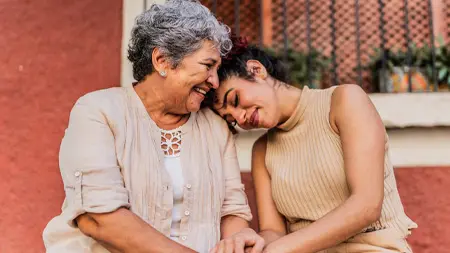 Deux femmes se tiennent les mains tandis que l’une d’elles appuie sa tête sur l’épaule de l’autre.