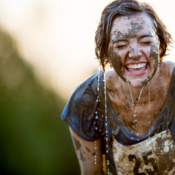 Une femme couverte de boue rit aux éclats durant une course à obstacles.