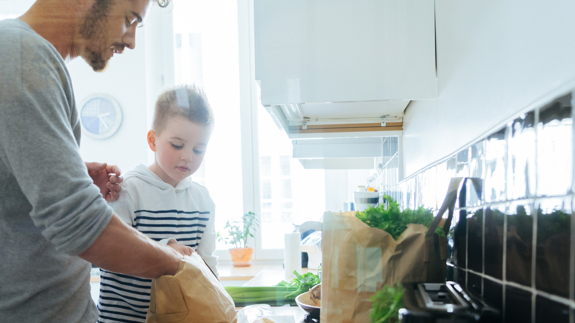 Dans une cuisine, un père et son fils rangent des articles d’épicerie.