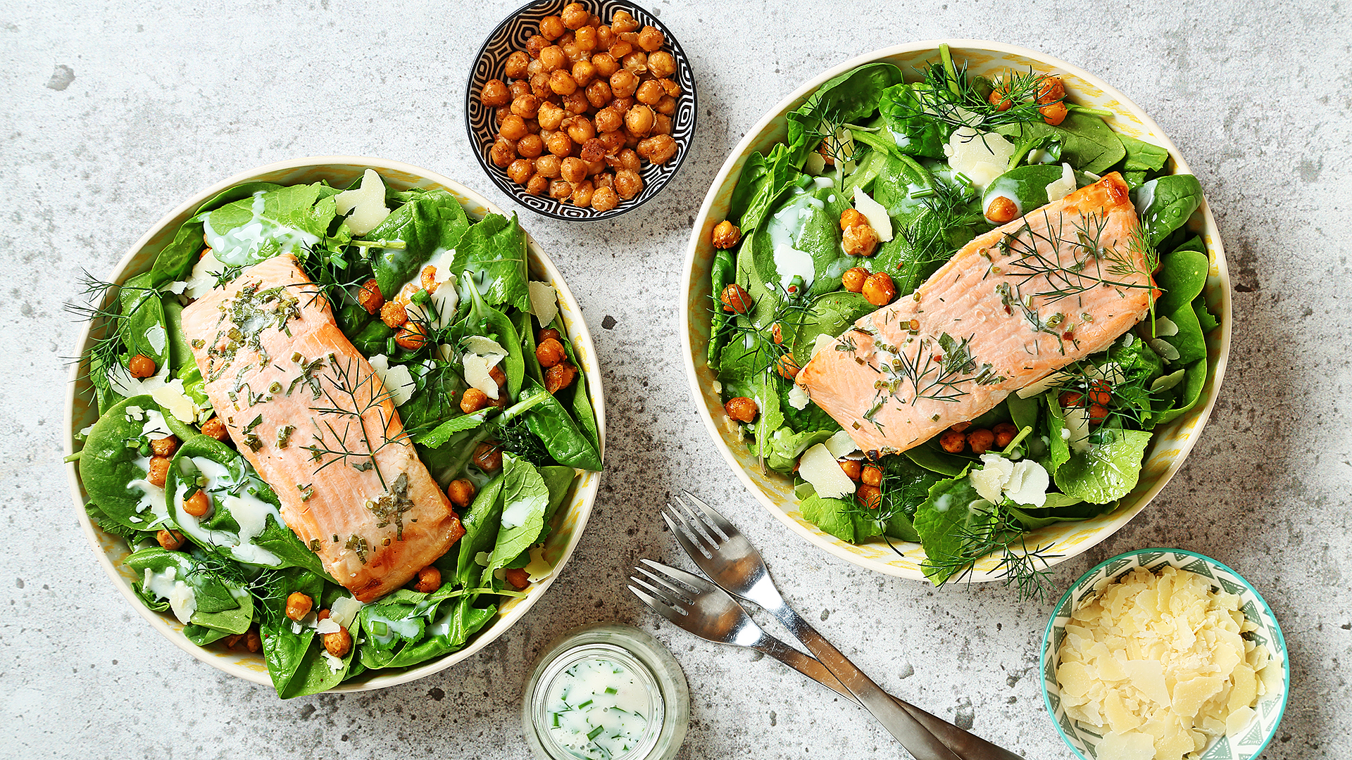 Salade de pois chiches au chou frisé à la truite avec des ustensiles en argent et des bols de pois chiches, vinaigrette et parmesan sur le côté.