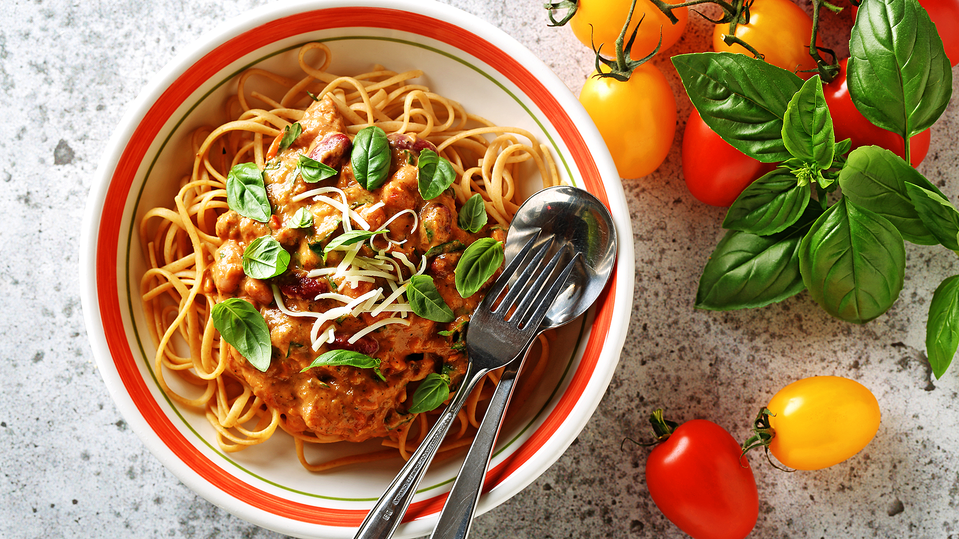 Rôti sauce tomate Linguini dans un bol avec l'argenterie et les tomates entières et des coupures de basilic sur le côté.