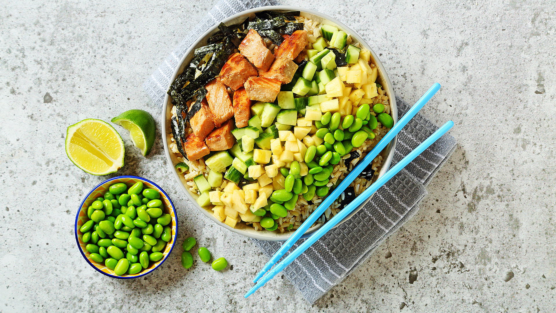 Salade style saumon poke dans un bol avec des baguettes bleues et edamame et citron vert sur le côté