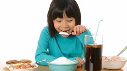 Une fille souriante prétend manger une grande cuillerée de sucre d'un bol bleu