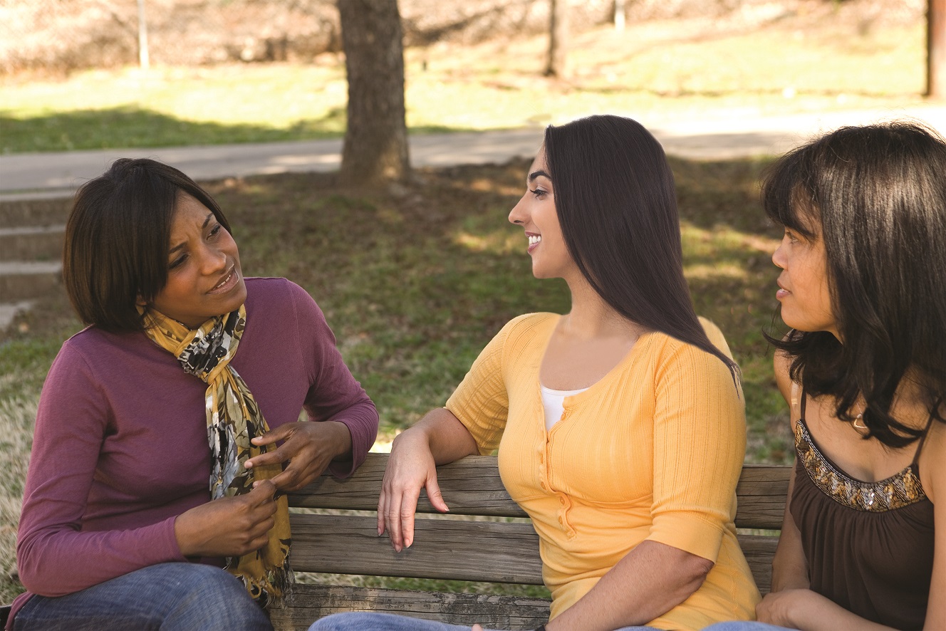 Trois femmes sont assises sur un banc de parc et discutent.