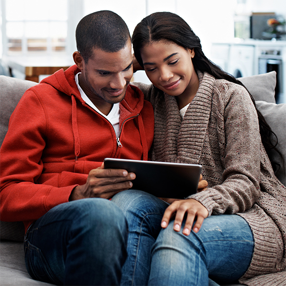 Couple assis sur un canapé tenant une tablette