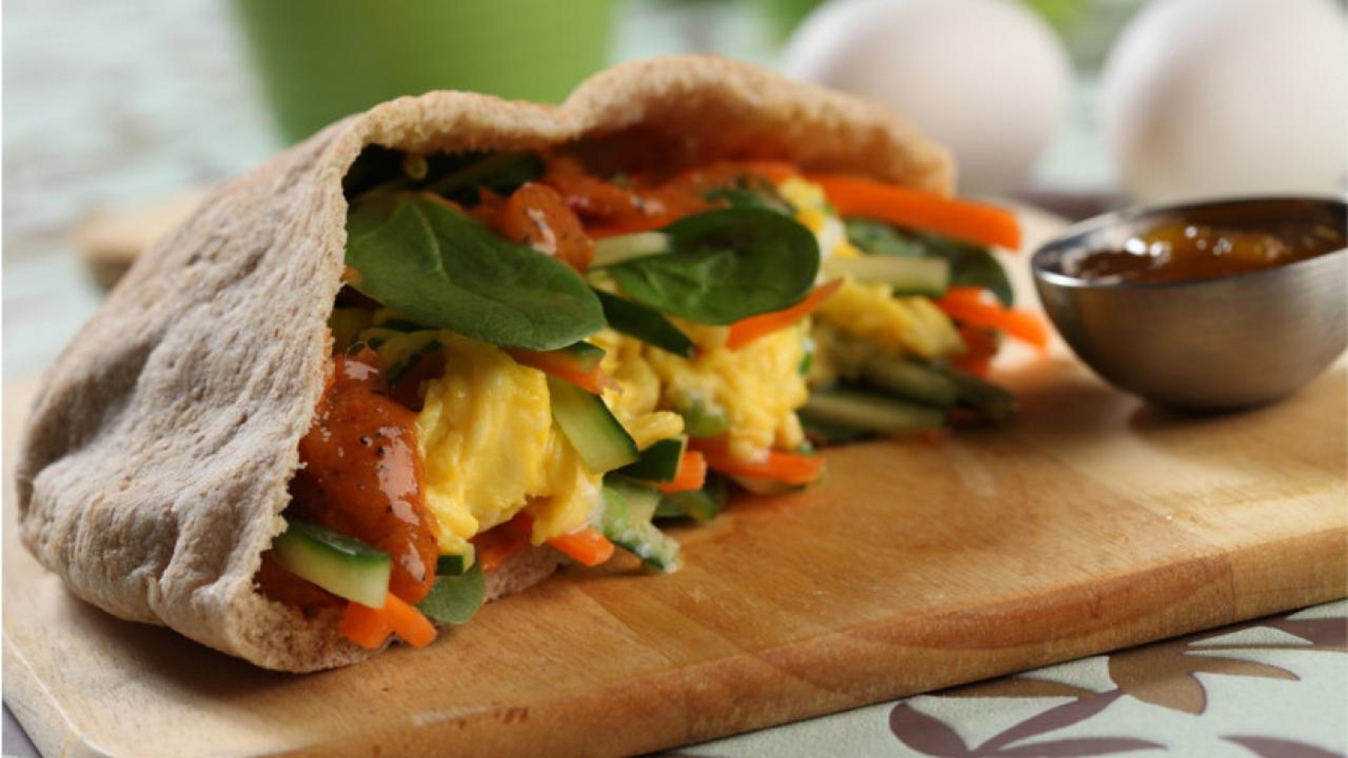 Un pita de blé entier coupé en deux et rempli de légumes et d'œufs au curry, présenté sur une planche à découper et un côté de sauce.