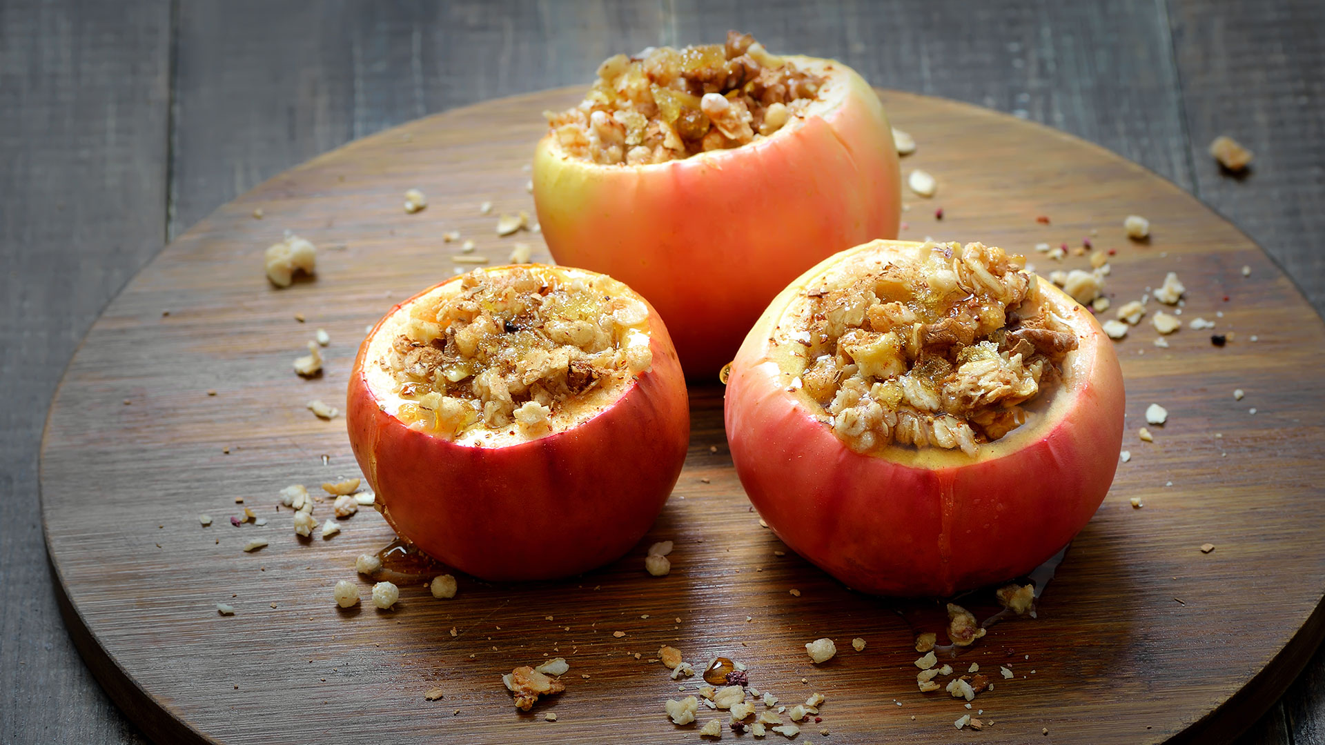  Trois pommes rouges cuites au four sur une planche de bois fourrée à la granola.