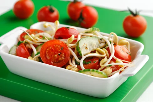 Salade de tomates et fèves germées dans un plat blanc sur une planche verte