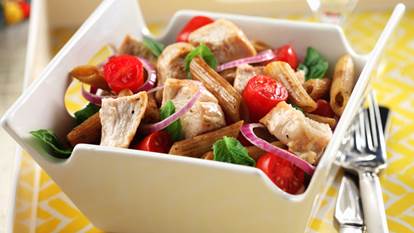 Salade de pâtes au poulet bistro dans un bol carré blanc avec une fourchette sur une nappe jaune